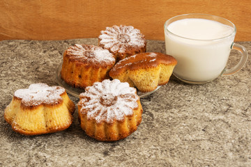 Homemade muffins sprinkled with powdered sugar on a gray background. Nearby is a glass cup with milk