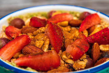 A smoothie bowl with oats, almond milk, almond yogurt, spinach, banana, berries, sliced strawberries, grapes topped with crushed almonds, almonds, Ezekiel cereal and a splash of cinnamon 