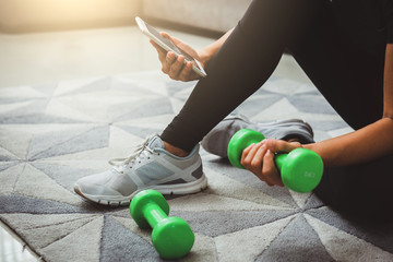 A sporty woman using smartphone during workout at home in the living room. Online personal trainer or on mobile phone.Sport and recreation concept.advice to stop coronavirus COVID-19 spreading.