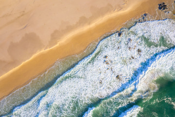 Fototapeta premium Top down aerial view of waves crashing into the beach with beautiful green water and soft sand