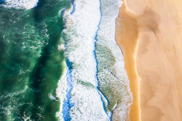 Fototapeta na wymiar Top down aerial view of waves crashing into the beach with beautiful green water and soft sand