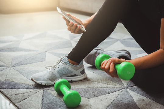 A sporty woman using smartphone during workout at home in the living room. Online personal trainer or on mobile phone.Sport and recreation concept.advice to stop coronavirus COVID-19 spreading.