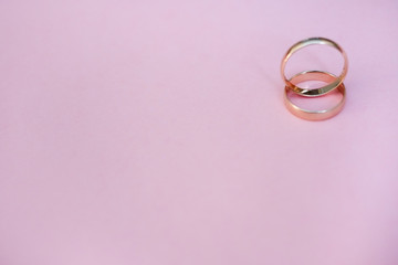 Two gold wedding rings of the bride and groom, husband and wife lie in the form of an infinity sign on a pink background, front view: wedding concept, Valentine's day