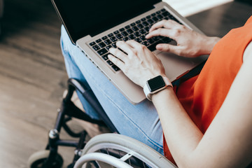 Woman in a wheelchair at home with a laptop on her lap, hand close up, unrecognizable man.