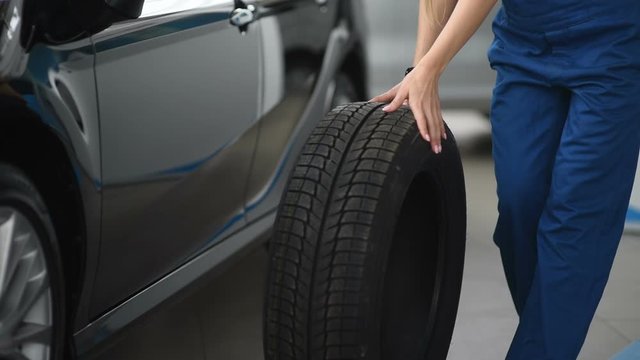 A mechanic woman rolls a new wheel for a car in a garage. Replacement of winter and summer tires.