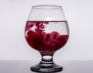 Colored ink spreads over a glass of water