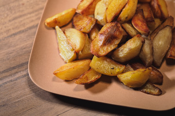 Baked crispy potatoes in a brown plate on a wooden table