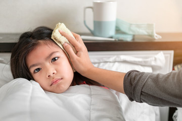 Obraz na płótnie Canvas Asian mother take cool towel for reduce high fever on sick girl forehead on bed at morning time,Sick child with high fever, Selective focus, Healthy and infection concept