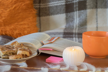 A cozy home still life from a 19th-century book by Jane Austen, coffee, candles and cookies on a plaid background.