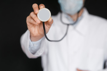 Male Doctor on a black background with a stethoscope in his hands close-up