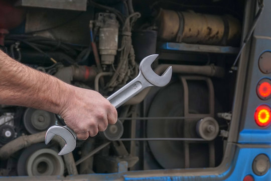    A large wrench in the hand of a car mechanic on the background of a car motor.