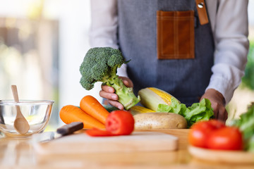 A woman chef holding and picking a fresh green broccoli from a vegetables tray on the table