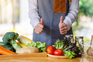 Closeup image of a female chef making and showing thumbs up hand sign while preparing fresh mixed vegetables to cook in kitchen