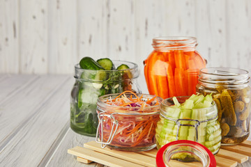 Fermented preserved vegetarian food concept. Sour sauerkraut, pickled carrots, pickled cucumbers, pickled celery in glass jars on a white wooden kitchen table. The concept of canned food. Copy space