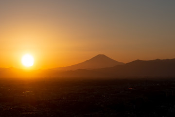 夕焼け・夕暮れ時、街並みの向こうに沈む太陽の夕日と富士山のシルエット