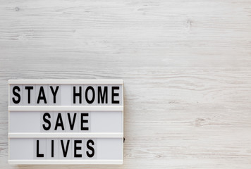 'Stay Home Save Lives' words on a lightbox on a white wooden surface, top view. Overhead, from...