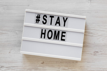 'Stay home' words on a lightbox on a white wooden surface, top view. Overhead, from above, flat lay.