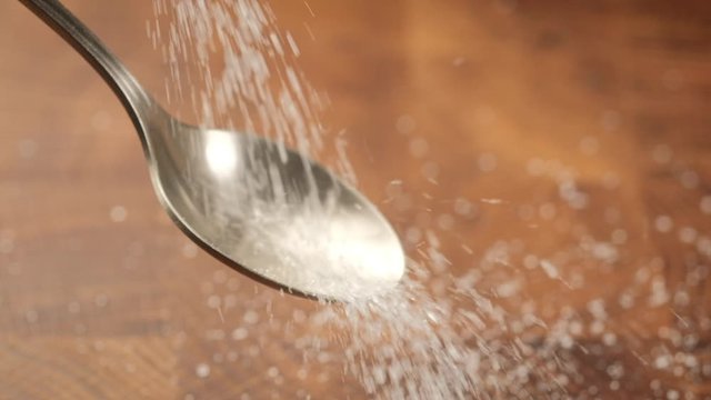 Stack of footage: White sugar fall through teaspoon down on a brown wood background. Slow motion. HD