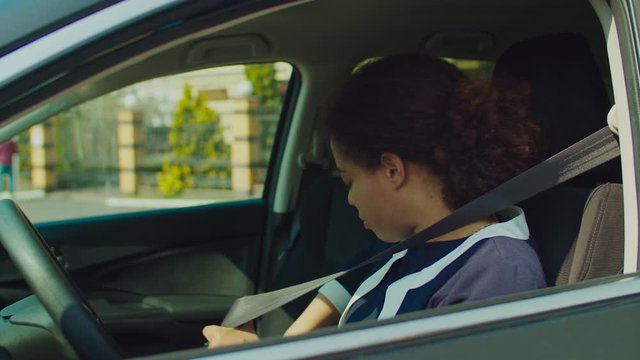 Beautiful african american female driver in formalwear fastening seat belt in car for safety drive. Responsible pretty african woman seating in driver's seat and buckling up seat belt before driving.