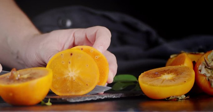 Male hand with a knife cut persimmons into round pieces on a stone Board.