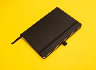 Black notebook isolated on yellow background.