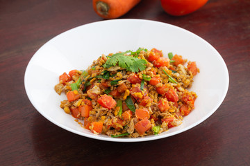 Homemade Scrambled eggs with carrots and tomatoes in white plate on wooden table.