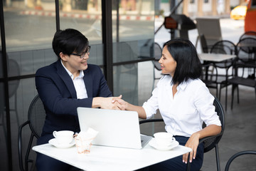 Asian and Caucasian business man working with laptop computer and shaking hands after concluding the agreement at a co-working space, Coffee shop. business success concept