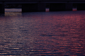 Dreamy bright colorful surface of water with little waves of purple, pink, blue color and black squares on sunset, abstract background, texture.