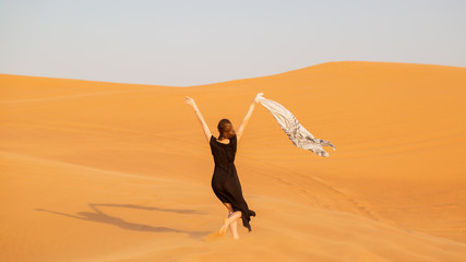 A girl walks on the sand in a deserted desert. A woman in a black dress with a cloth in her hands in a strong wind alone in the desert