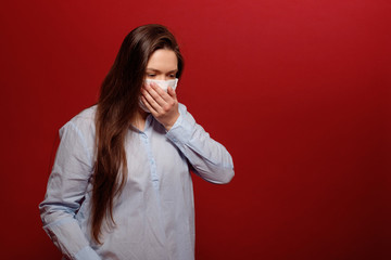 coronavirus pandemic, close-up portrait of young woman on red background in protective medical mask, sneezes