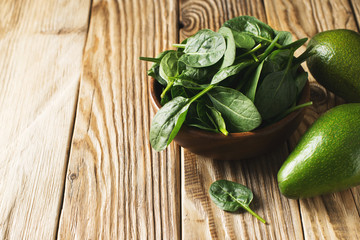 Baby spinach and avocado in wooden bowl on table, green healthy ingredient