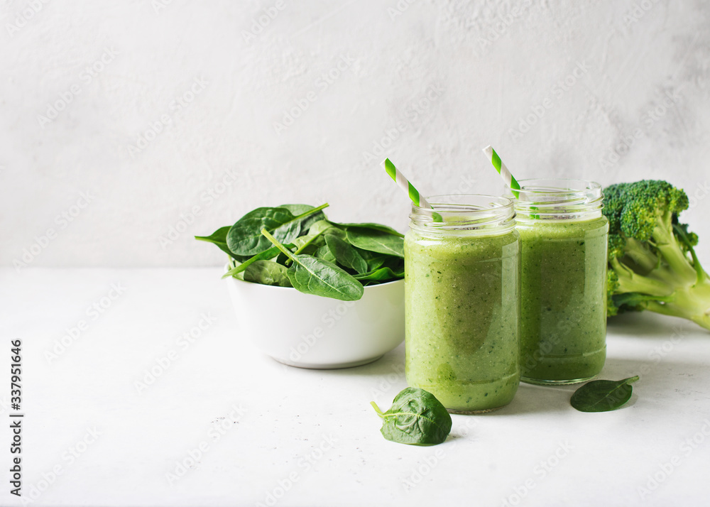 Wall mural green smoothie in glass jar with straw and spinach and broccoli on white background, top view,