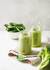 Green smoothie in glass jar with straw and spinach and broccoli on white background, top view,...