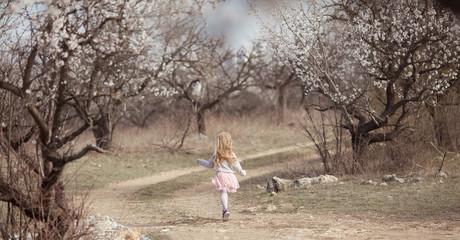 Happy beautiful girl runs in a flowering almond garden