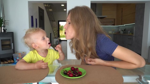 Loving mummy feeding her child boy with cherry berry at home. Mother kissing son