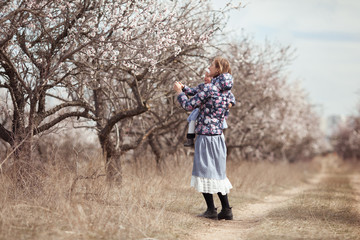 Portrait of happy mother and daughter on a background of almond trees in blossom, a woman and a child walk in the spring garden