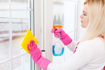 Woman cleaning windows at home with detergents cleaner