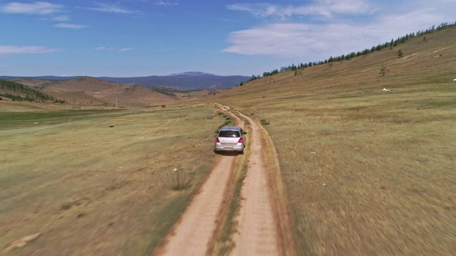 Aerial footage filmed with drone of pickup car riding in steppe. the car travels along the steppe to Siberia, roads laid along the Baikal island through the grassy hills.