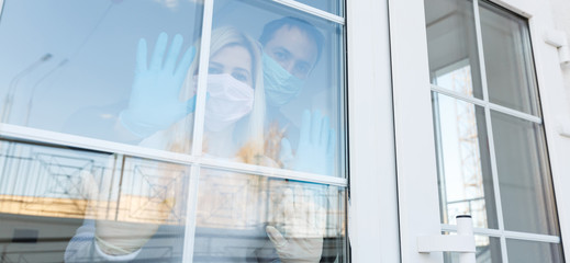 Fototapeta na wymiar Stop infection. woman shows stop gesture through glass door there is no exit. girl wears a protective mask against infectious diseases flu in a public place. The concept of health, the quarantine.
