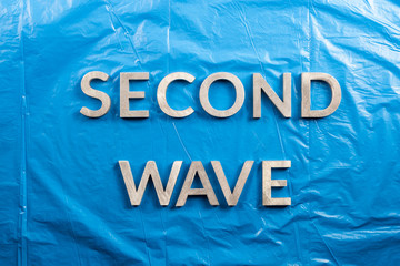 the words second wave laid with silver metal letters over crumpled blue plastic film background