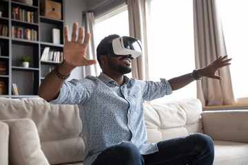 Overjoyed young mixed race guy wearing vr headset, enjoying spending leisure free time in virtual reality. Excited millennial multiracial man playing online game simulation, testing modern purchase. - Powered by Adobe