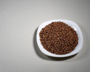 Raw buckwheat in a white plate on a gray background. Ingredient for cooking. View from above.