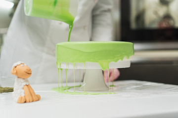 Pastry cook prepares a cake of green, watering it with icing