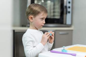 Little blond boy prepares holiday cookies in the kitchen and plays with baking dishes, he frowns