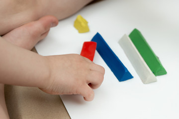 red bar of plasticine in the hand of a child. multi-colored pieces on the background