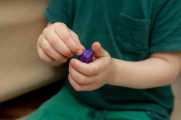 a three-year-old child holds in his hands a purple piece of plasticine. modeling. development of fine motor skills in children