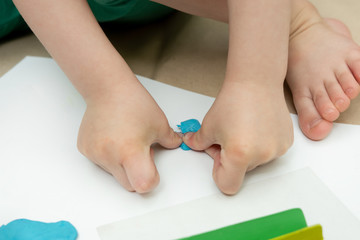 Obraz na płótnie Canvas children's hands sculpt blue plasticine on white paper. children's creativity. close-up.
