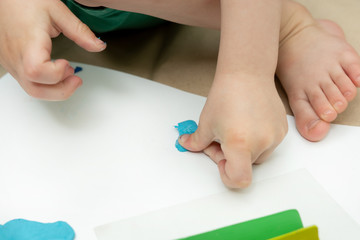 children's hands sculpt blue plasticine on white paper. children's creativity. close-up.