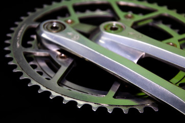 Detail for a road bike on a black background. Old school crankset and chainrings close-up. Soft side light with a slight yellow tint. Bicycle repair.