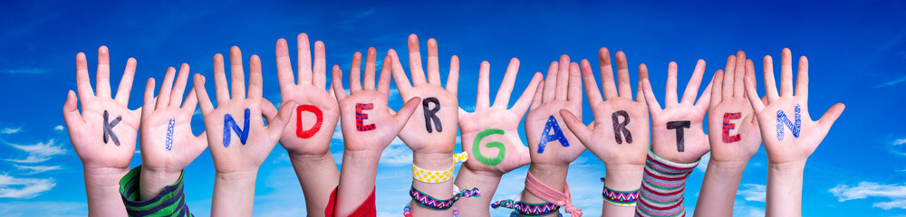 Children Hands Building Colorful German Word Kindergarten Means Kindergarden. Blue Sky As Background
